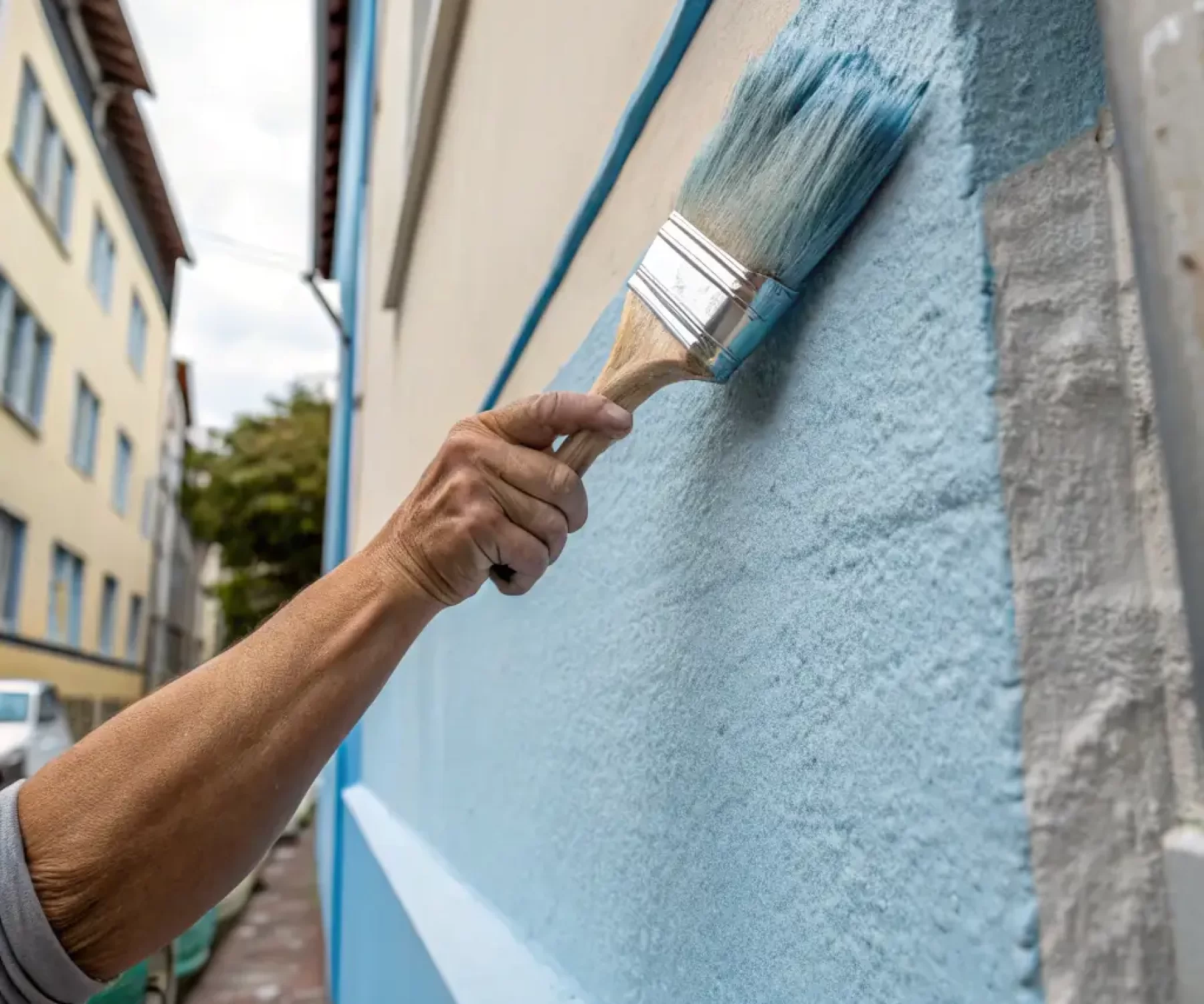 A close-up shot of a painter's hands expertly applying paint to a wall with a brush, showcasing precision and attention to detail.